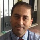 Portret mężczyzny w koszuli w paski i krawacie, siedzącego na tle segregatorów w biurze.